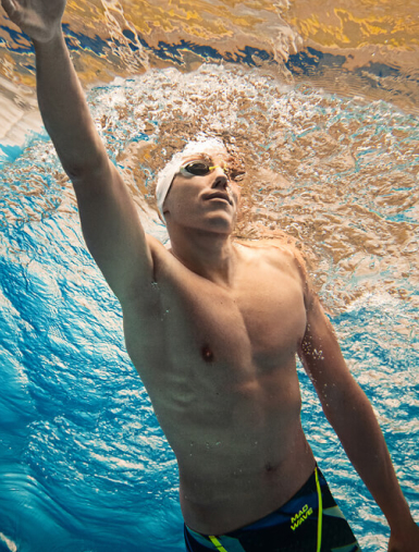 A man doing swimming in the water wearing a swimming suit and accessories from Mad Wave.